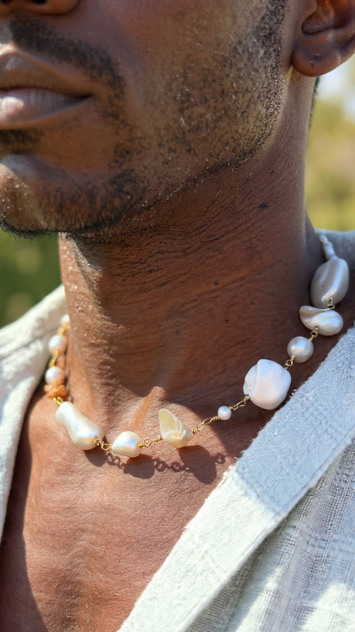 A close-up of a baroque pearl necklace with a brown deerskin leather tie, worn around the neck and catching natural light.