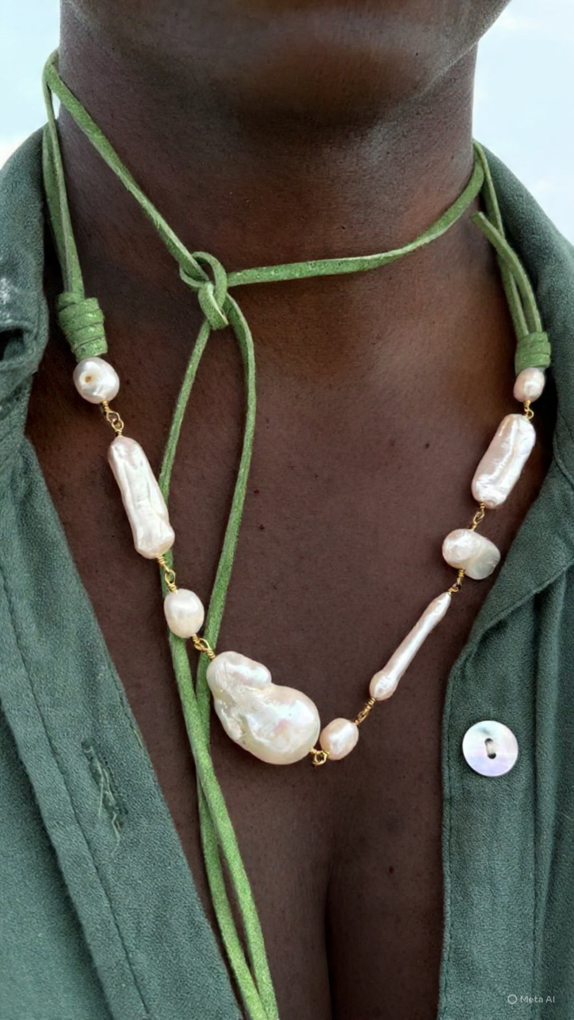A close-up of a green deerskin leather wrap necklace adorned with freshwater and baroque pearls, shown tied around the neck and draped down the chest.