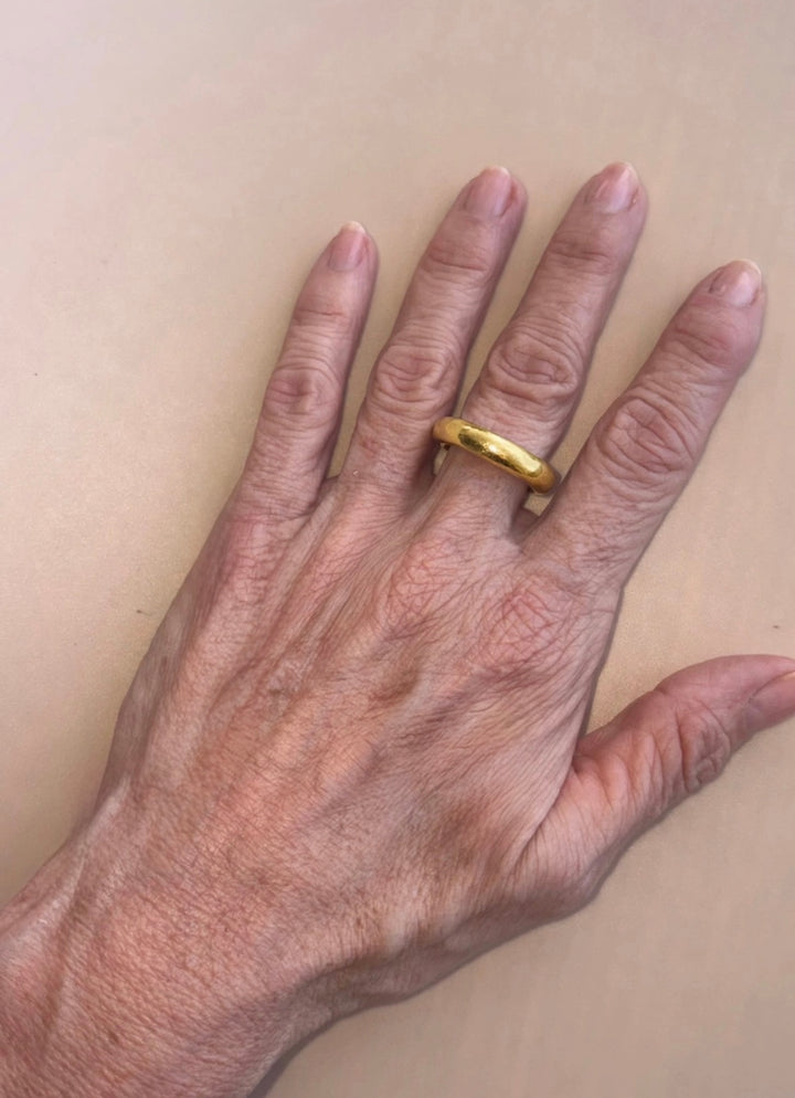 Ring One, a rounded 18K gold band, worn on the hand against a neutral beige background.