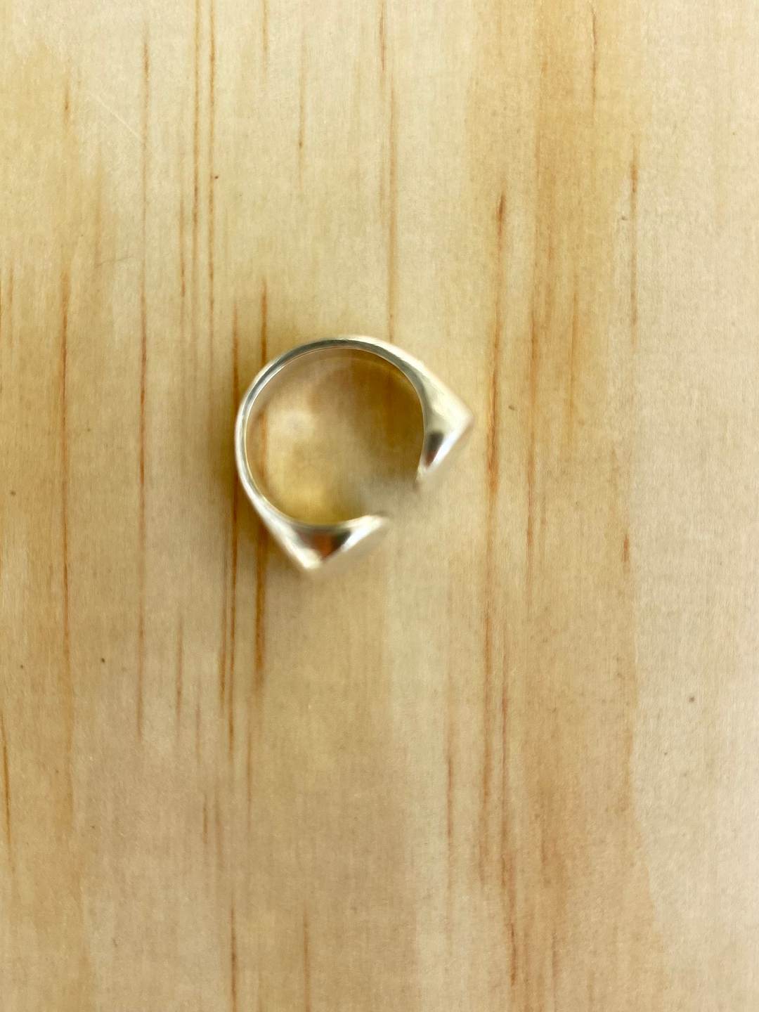 Overhead view of the sculptural sterling silver Dot Ring by Jewelry One of a KIND, showing its open circular band and tapered ends against a natural wood background.