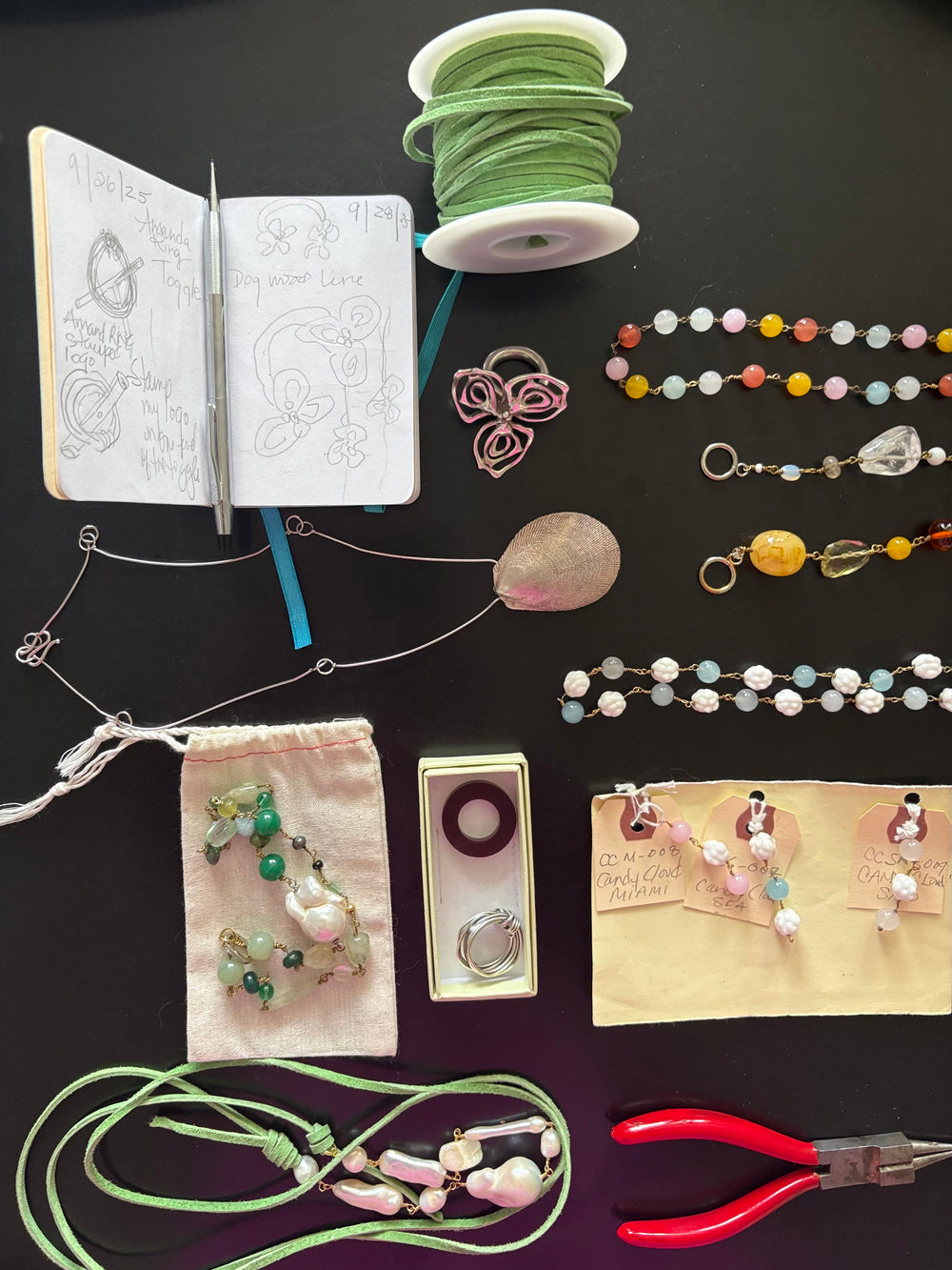 Jewelry-making supplies including beads, tools, and a notebook on a dark surface. With jewelry collection included. 