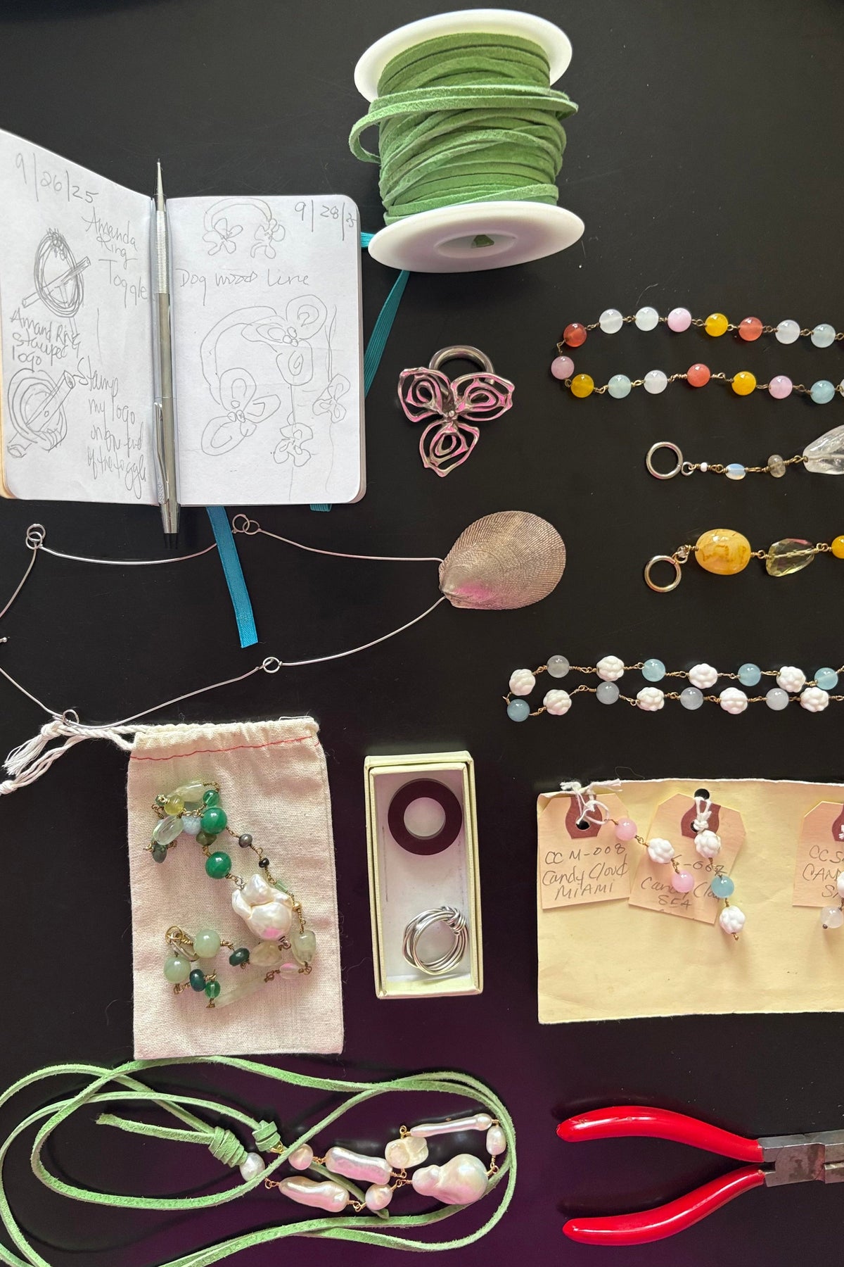 Jewelry-making supplies including beads, tools, and a notebook on a dark surface. With jewelry collection included. 
