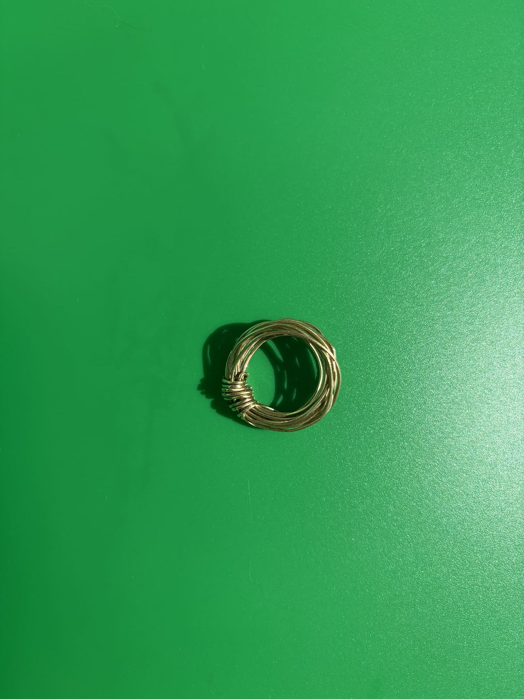 Brass knot ring handcrafted from a single wire, shown on green background. Survivor-made ethical jewelry symbolizing strength.