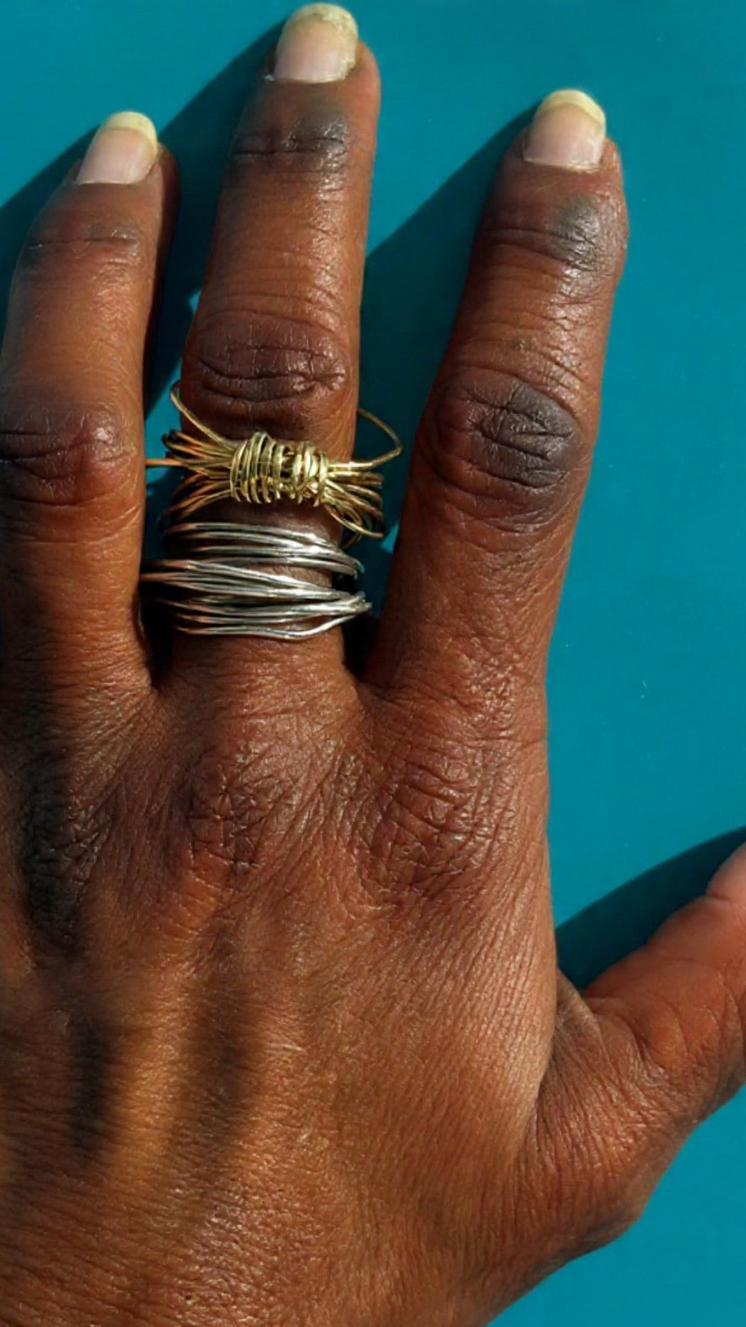 Hand wearing a silver and gold wire ring against a blue background
