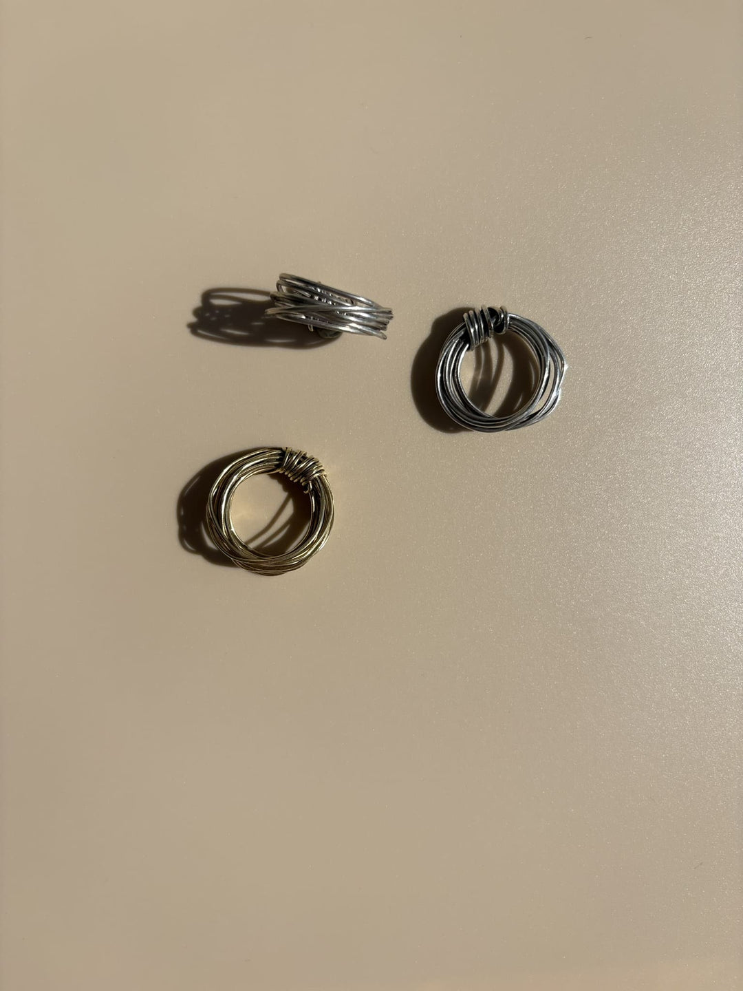 Brass and Fairmined sterling silver rings handcrafted by survivors from single 18-gauge wires, each formed into a knot without solder. Ethical luxury jewelry by Jewelry One of a KIND, symbolizing unbroken strength and resilience.