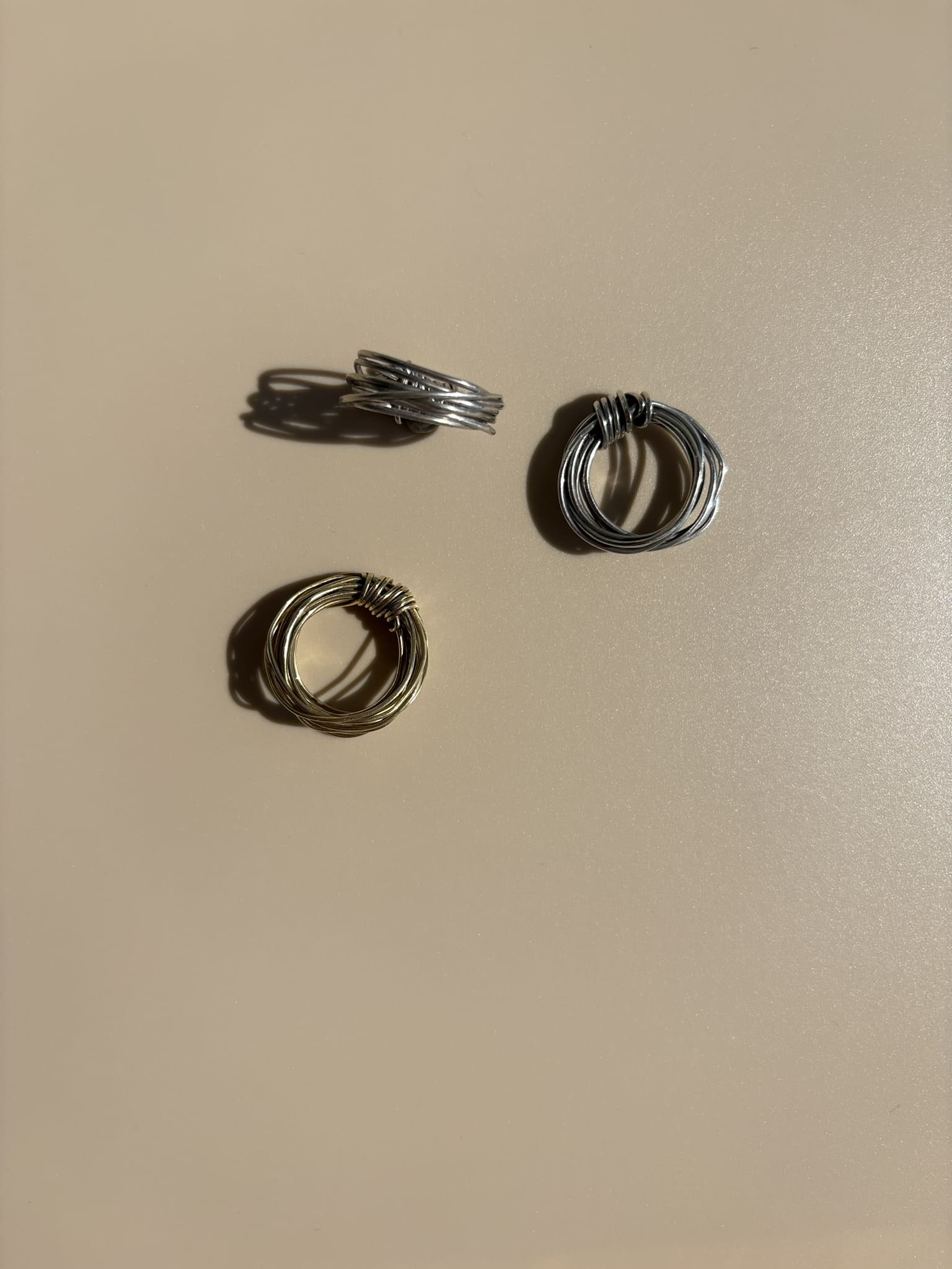 Brass and Fairmined sterling silver rings handcrafted by survivors from single 18-gauge wires, each formed into a knot without solder. Ethical luxury jewelry by Jewelry One of a KIND, symbolizing unbroken strength and resilience.