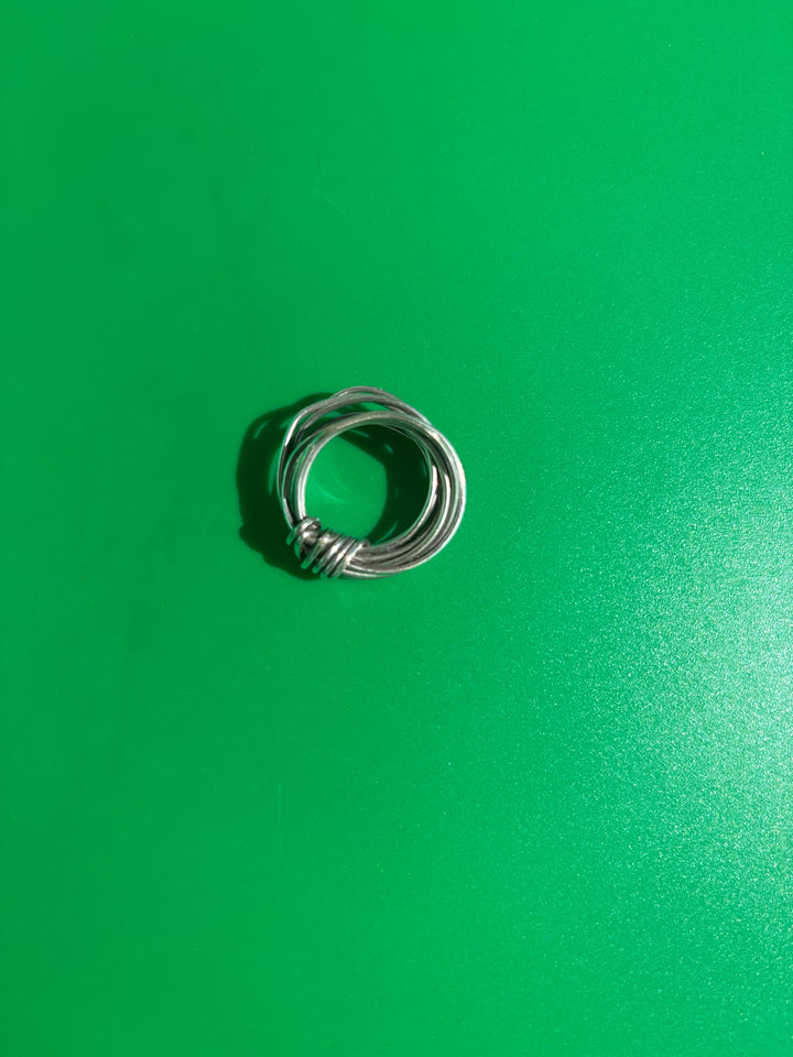 Fairmined sterling silver knot ring hand-wrapped from 18-gauge wire, on green background. Survivor-made ethical jewelry of resilience.