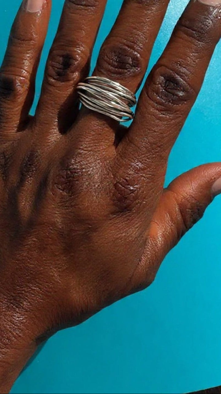 Hand wearing a sterling silver ring against a blue background. Survivor-made ethical jewelry symbolizing resilience.