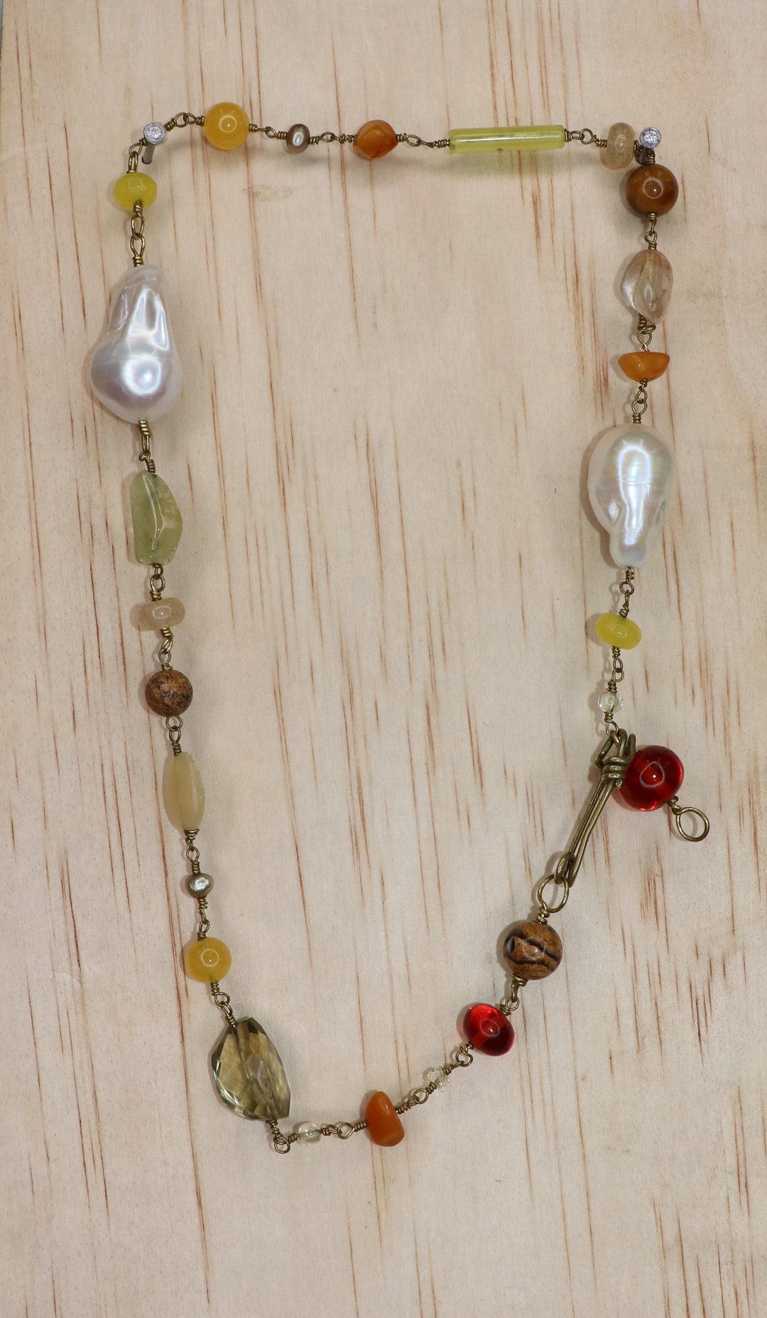 Emilia Necklace featuring two large freshwater baroque pearls, yellow, amber, and honey-toned gemstones, gold-toned links, and a signature handcrafted KIND Closure, displayed on a light wood block.