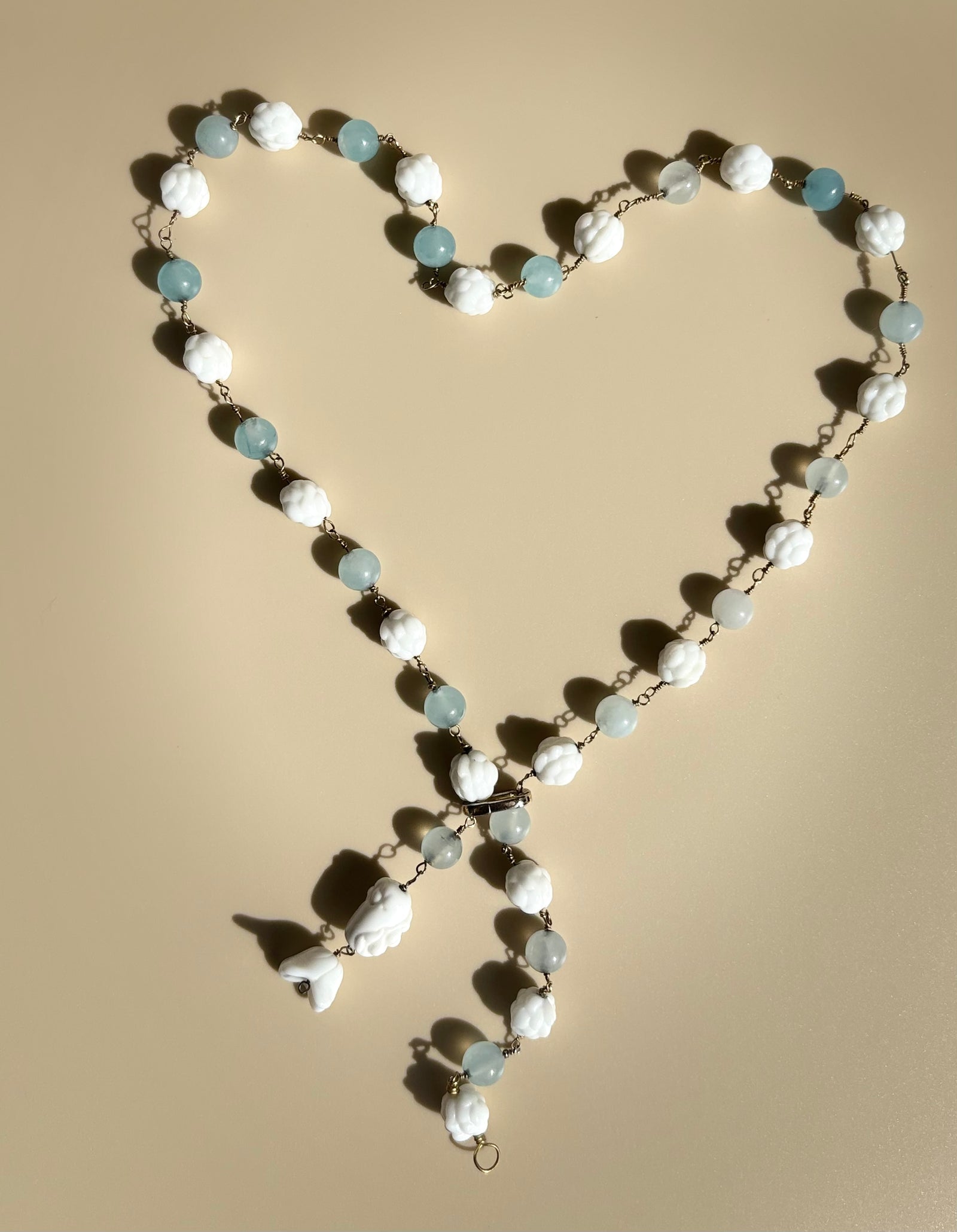 Baby blue quartz necklace displayed on beige surface. Survivor-made ethical jewelry representing memory and light.