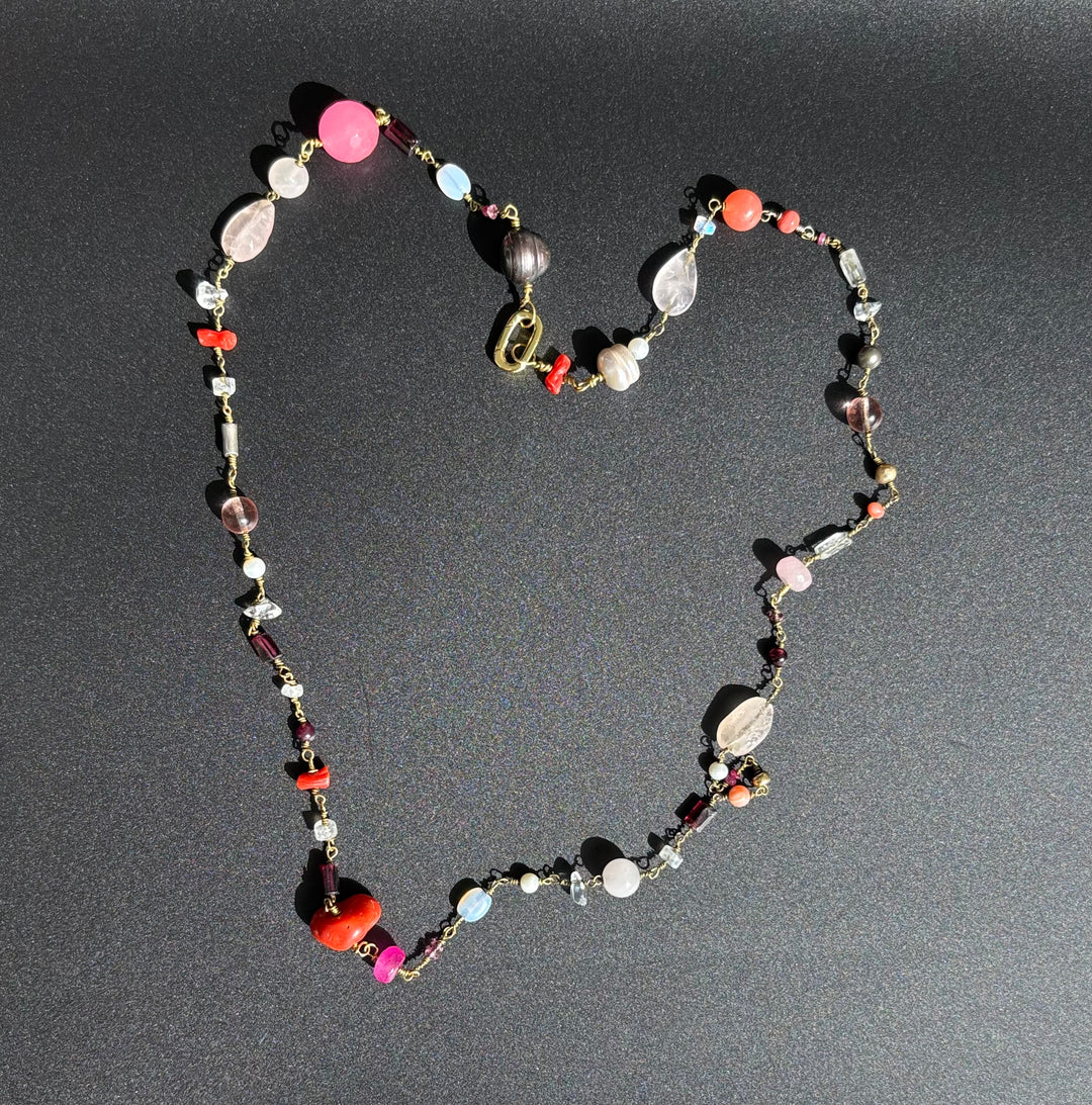 Pink gemstone necklace with  rose quartz, coral, and ruby, pearls and Swarovski crystals on black background. Survivor-made luxury jewelry.