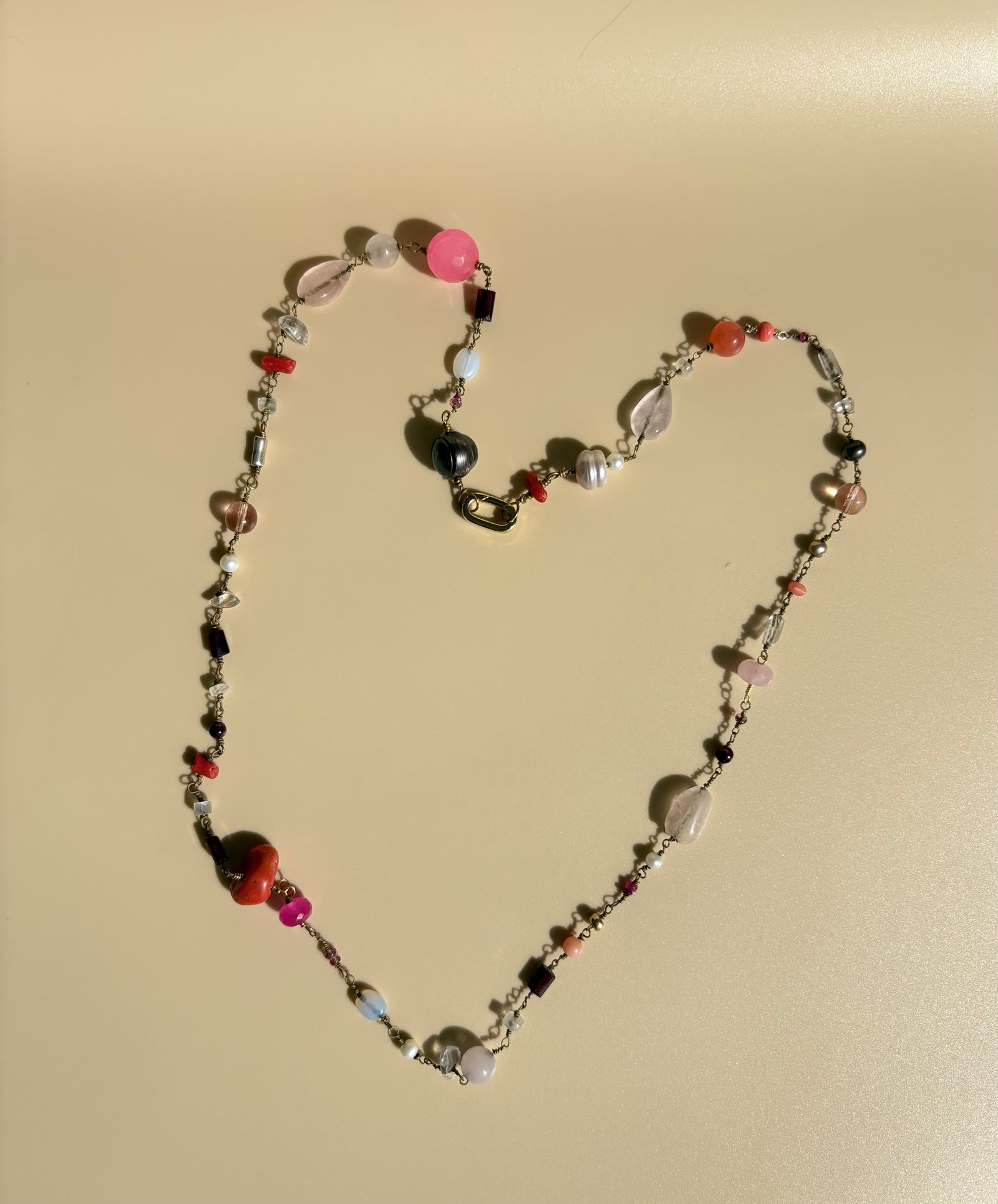 Rose quartz, pearl, pink dyed quartz, and coral necklace displayed on beige background. Survivor-made jewelry representing bold beauty and strength.