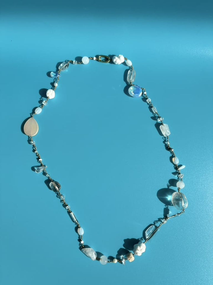 White gemstone necklace with moonstone and porcelain displayed on blue surface. Survivor-made ethical jewelry.