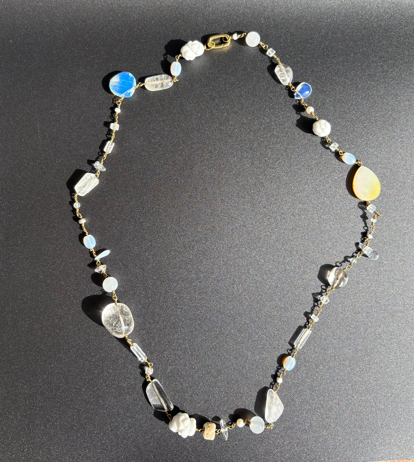 White gemstone necklace with pearls, porcelain, moonstone and coral on black background. Survivor-made jewelry symbolizing quiet resilience.
