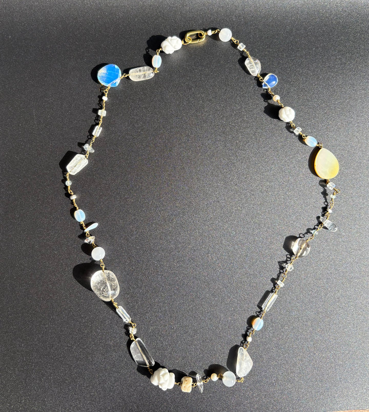 White gemstone necklace with pearls, porcelain, moonstone and coral on black background. Survivor-made jewelry symbolizing quiet resilience.