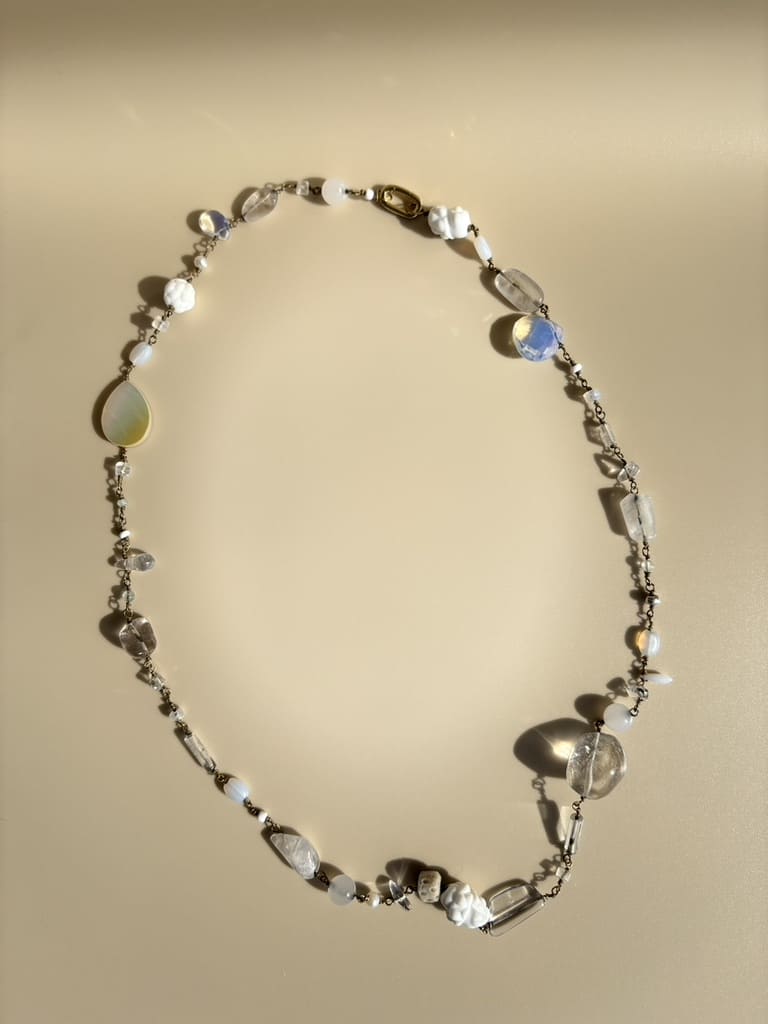 Quartz, rock crystal, and pearl necklace on beige background. Ethical handmade jewelry representing purity and peace.