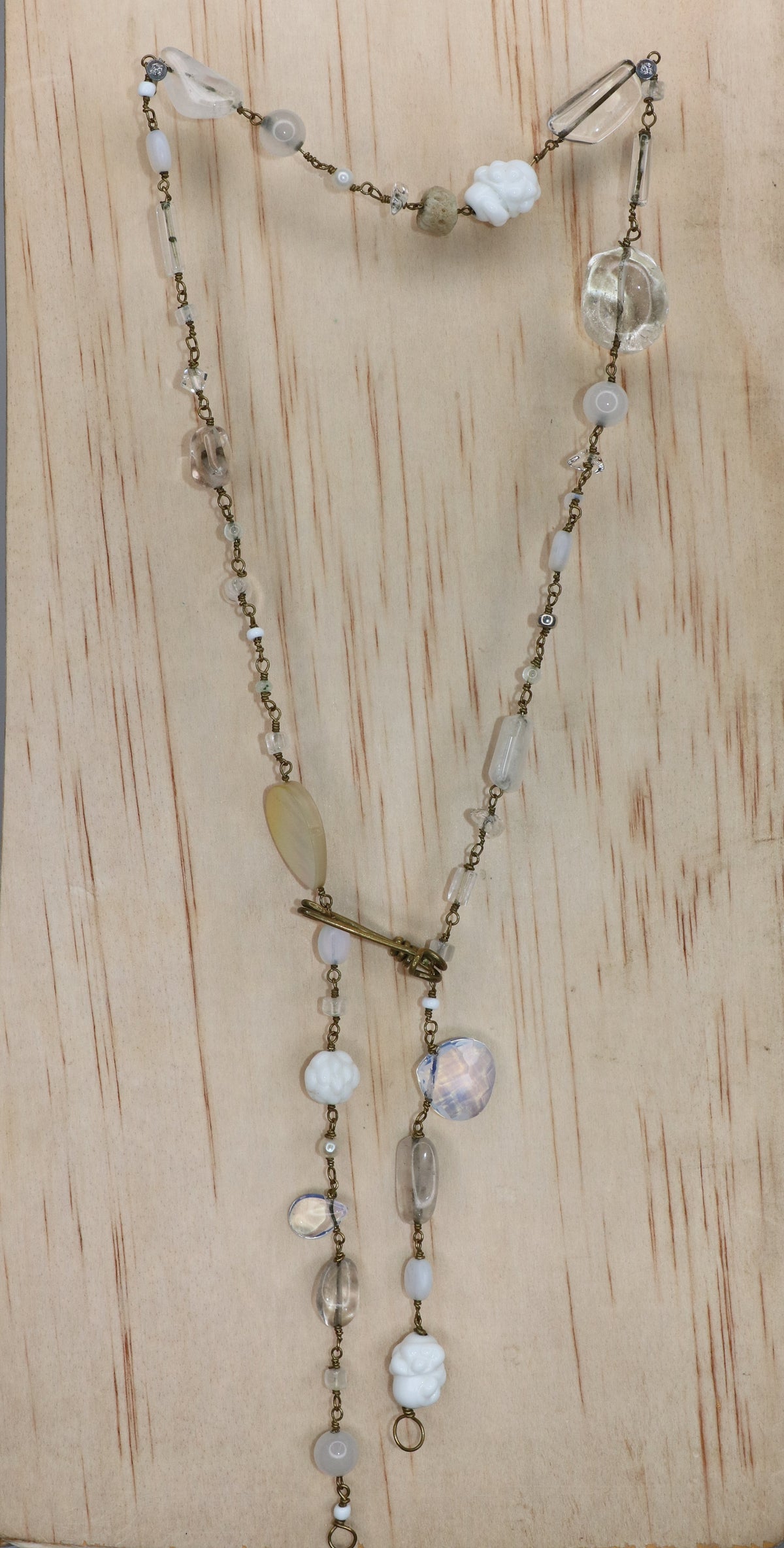 White gemstone necklace with pearls, porcelain, moonstone and coral on black background displayed on a light wood block.