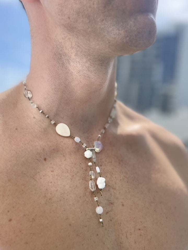 White gemstone necklace with pearls, mother-of-pearl, rock crystal and quartz on model’s neck. Survivor-made ethical jewelry expressing calm beauty.