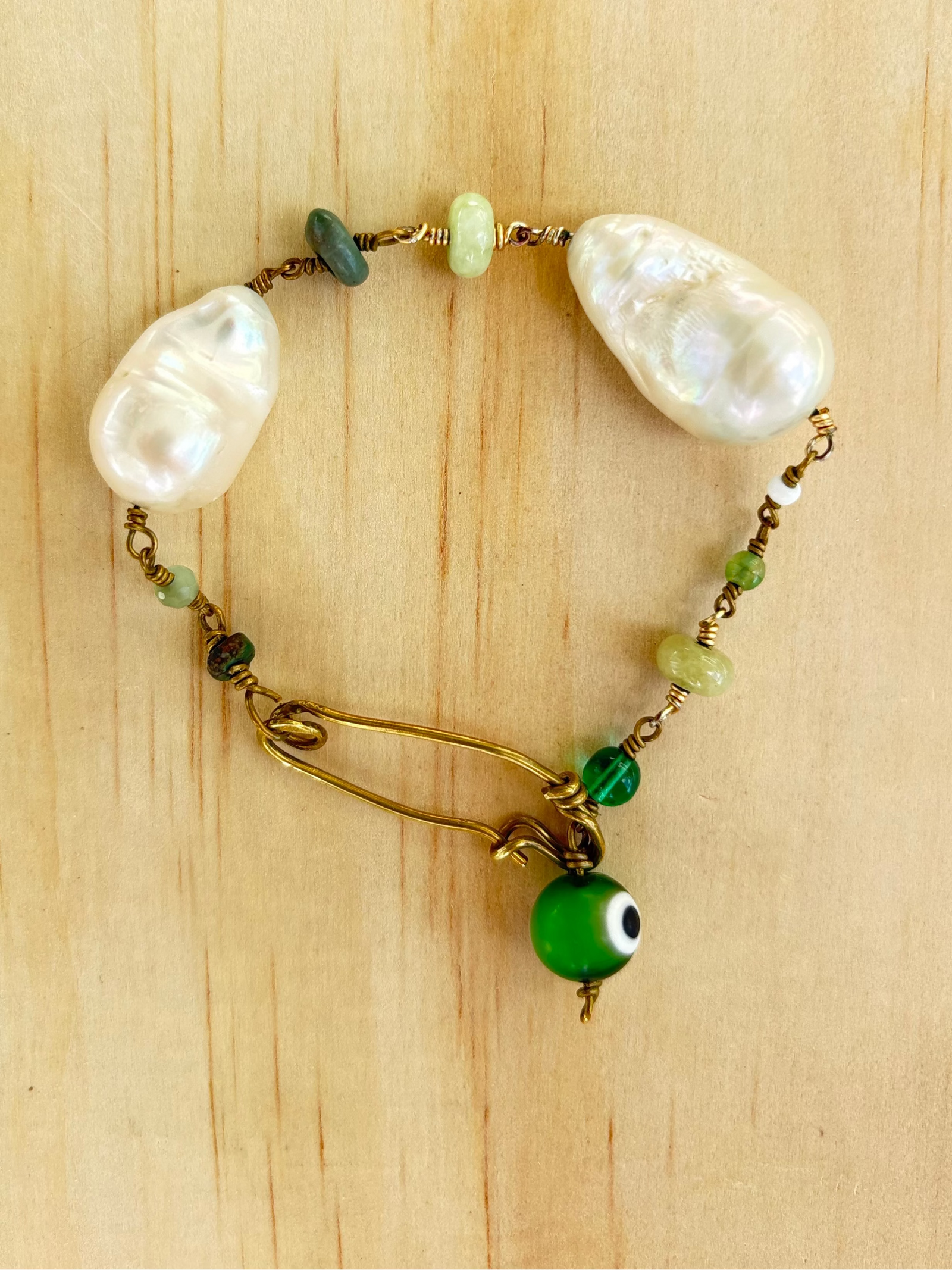 Marya collectible bracelet with two freshwater baroque pearls, individually selected green gemstones, Evil Eye charm, and handcrafted KIND Closure made out of brass. 