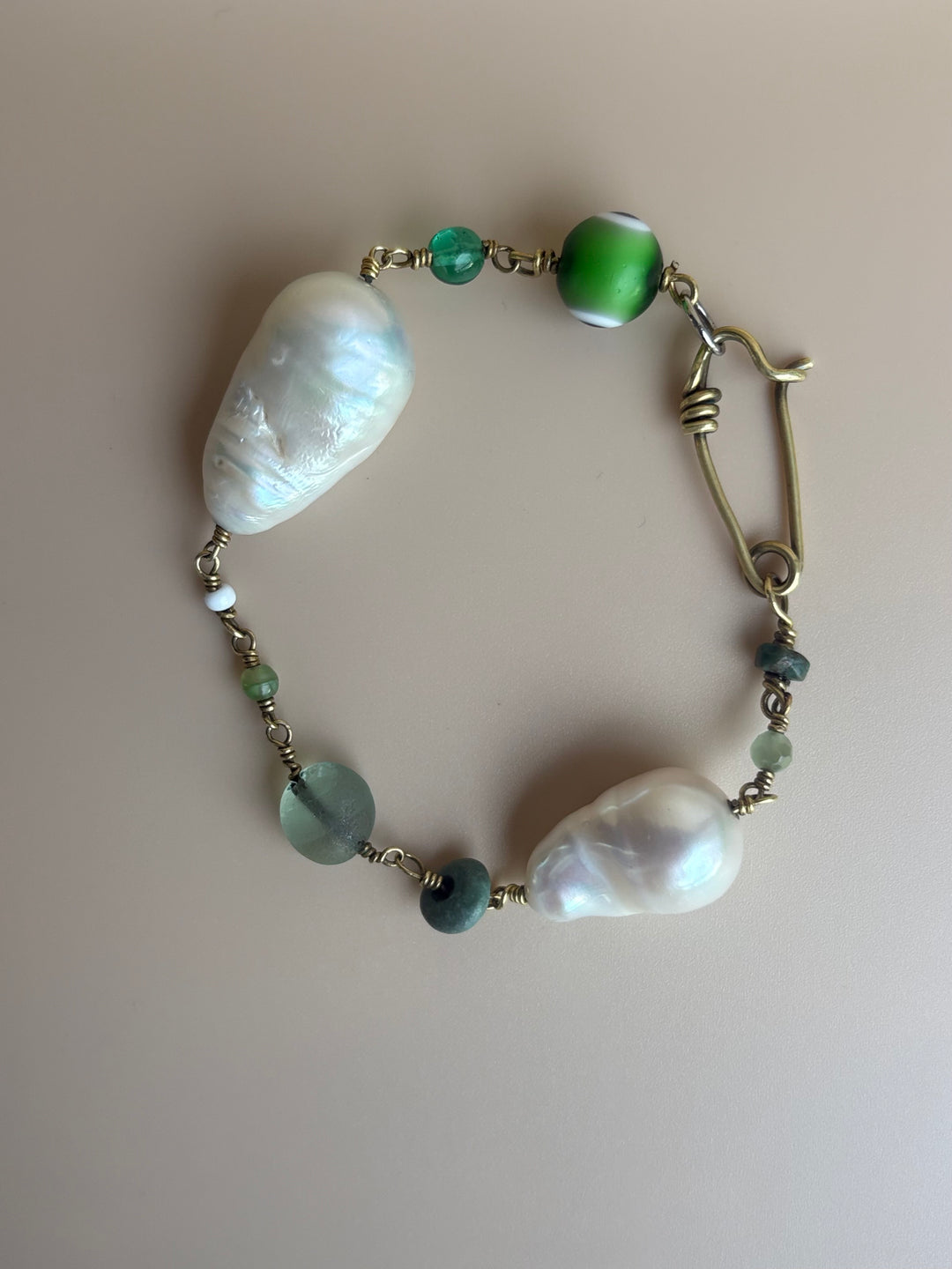 Baroque pearl bracelet with green Evil Eye and turquoise on blue background. Survivor-made luxury jewelry symbolizing empowerment.