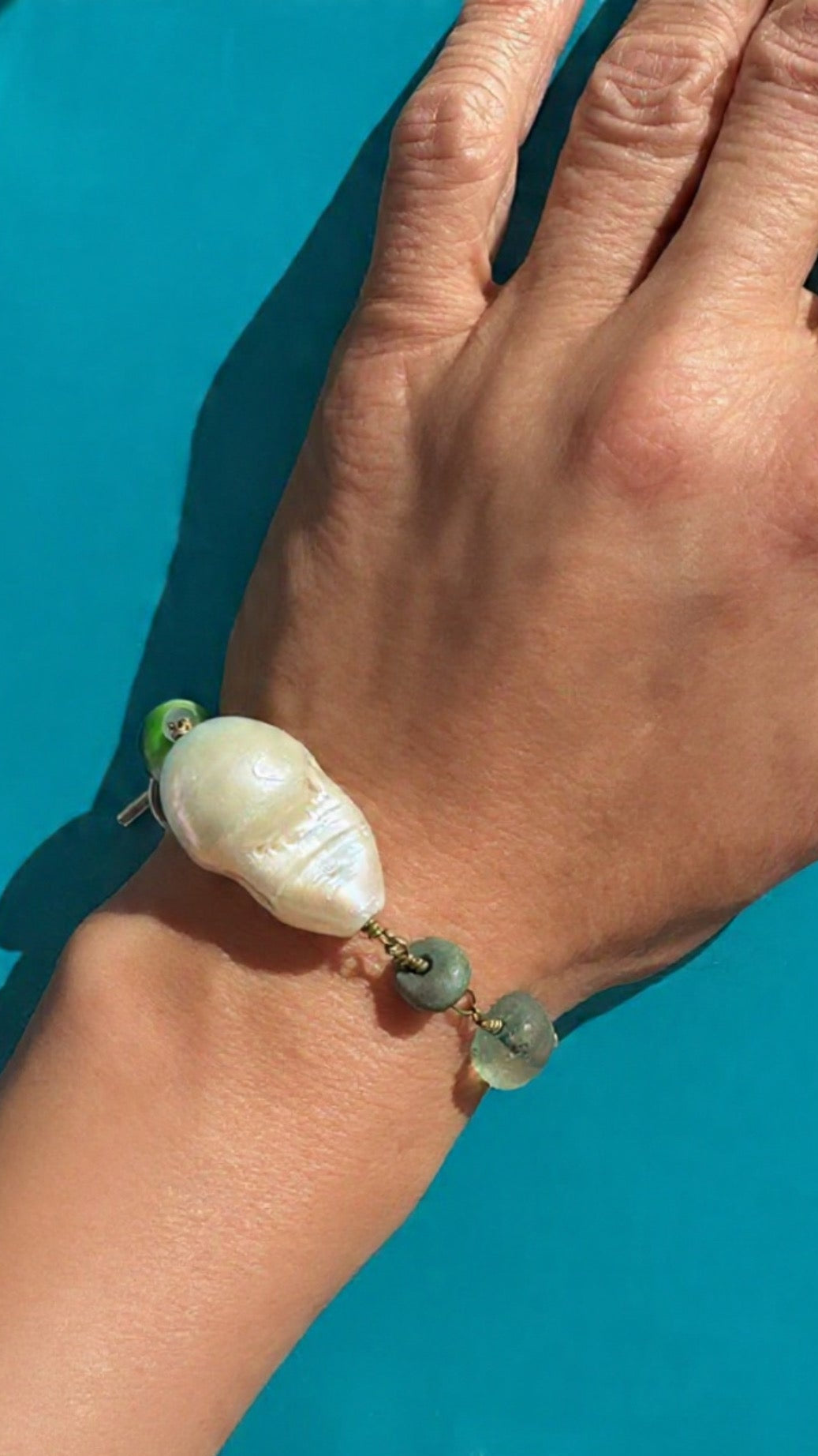 Close-up of a hand wearing a baroque pearl bracelet with a blue background