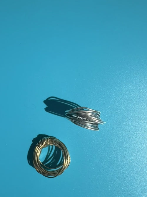 Brass and Fairmined sterling silver knot rings hand-wrapped from 18-gauge wire, displayed together on a blue background. Survivor-made ethical jewelry by Jewelry One of a KIND symbolizing strength and resilience.