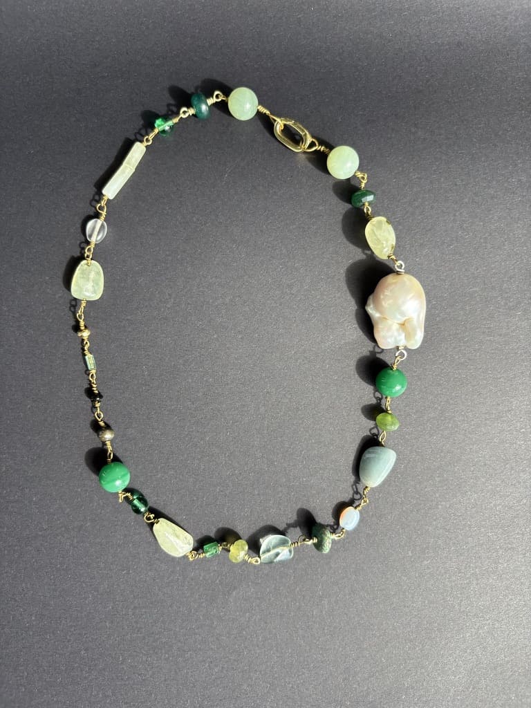 Black background: Green gemstone and baroque pearl necklace on black background. Survivor-made jewelry expressing resilience and strength.