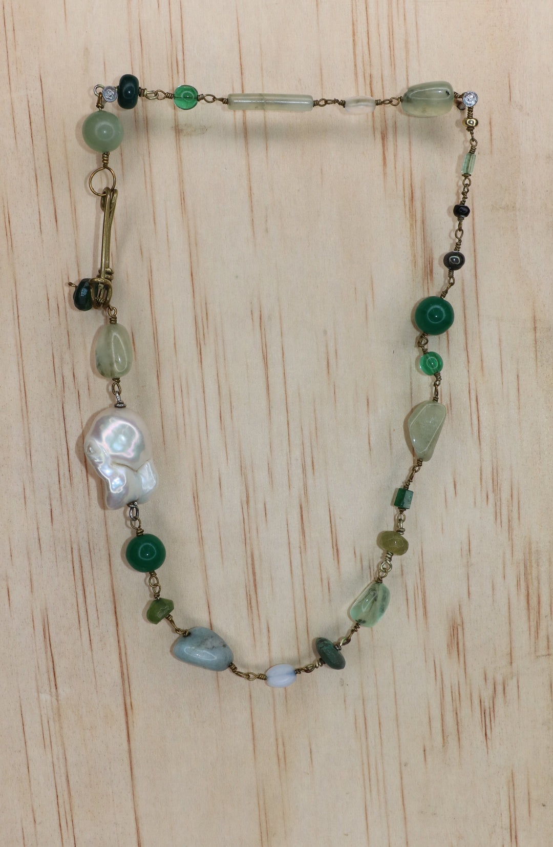 Rosa Necklace featuring a large freshwater baroque pearl, green and pale blue gemstones, and gold-toned links, finished with a signature handcrafted KIND Closure and displayed on a light wood block.