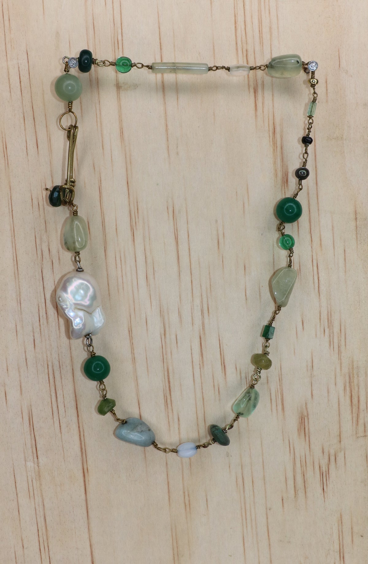 Rosa Necklace featuring a large freshwater baroque pearl, green and pale blue gemstones, and gold-toned links, finished with a signature handcrafted KIND Closure and displayed on a light wood block.