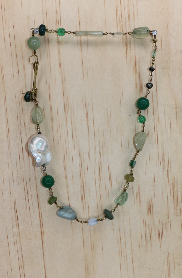 Rosa Necklace featuring a large freshwater baroque pearl, green and pale blue gemstones, and gold-toned links, finished with a signature handcrafted KIND Closure and displayed on a light wood block.