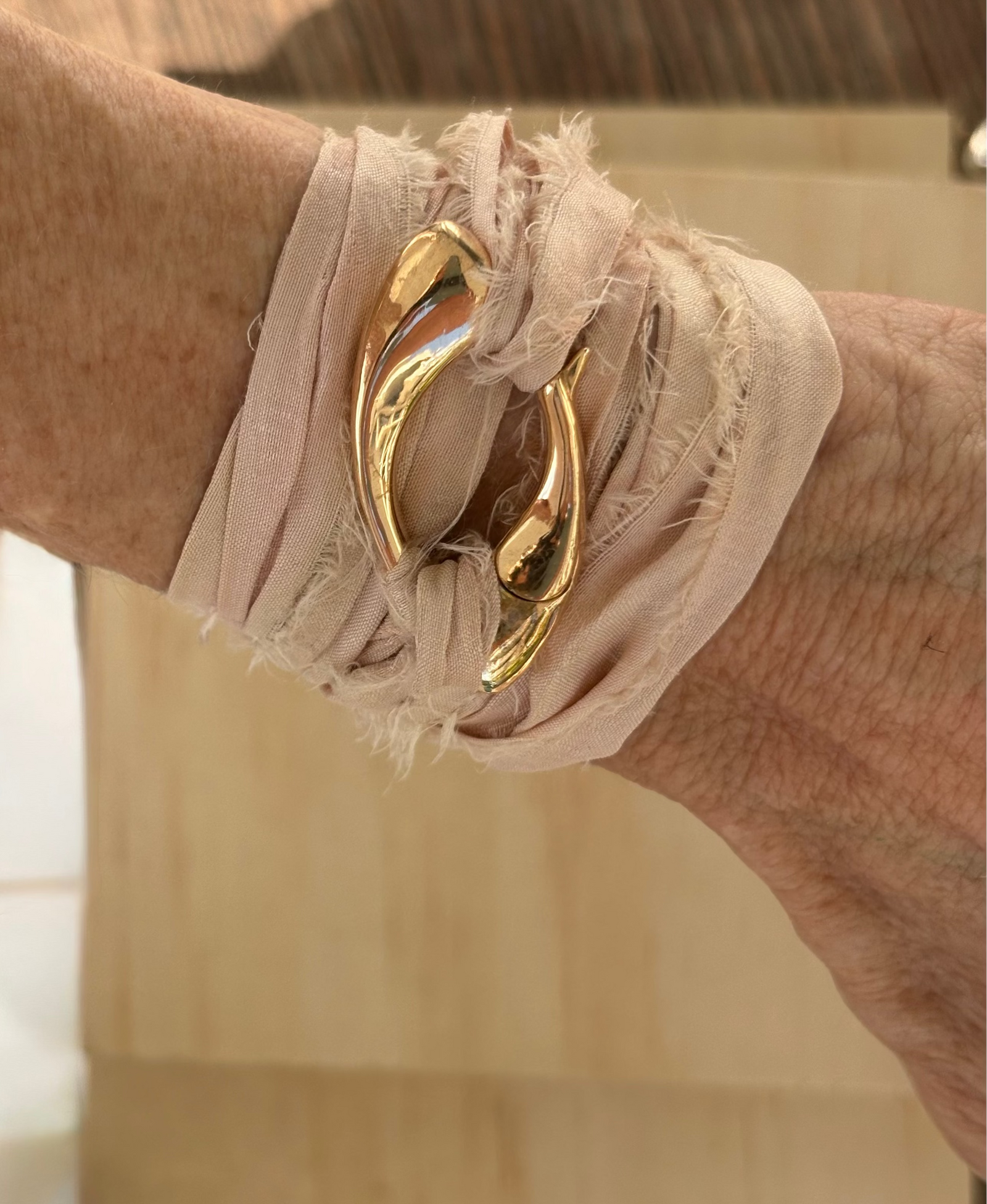 Close-up of a sculptural bronze Culebra closure wrapped in rose-colored, hand-dyed sari silk, worn around the wrist with  wooden background