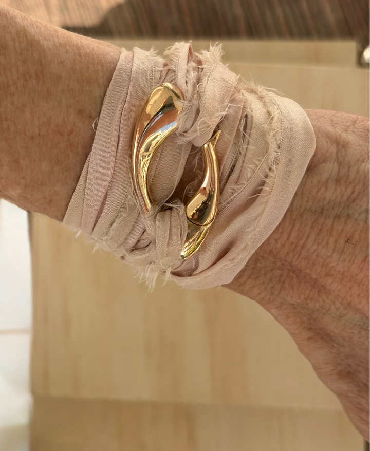 Close-up of a sculptural bronze Culebra closure wrapped in rose-colored, hand-dyed sari silk, worn around the wrist with  wooden background