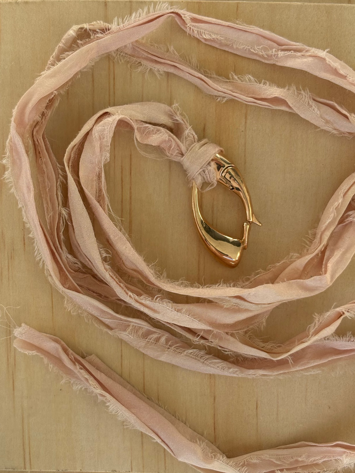 Close-up of a sculptural bronze Culebra closure onrose-colored, hand-dyed sari silk.