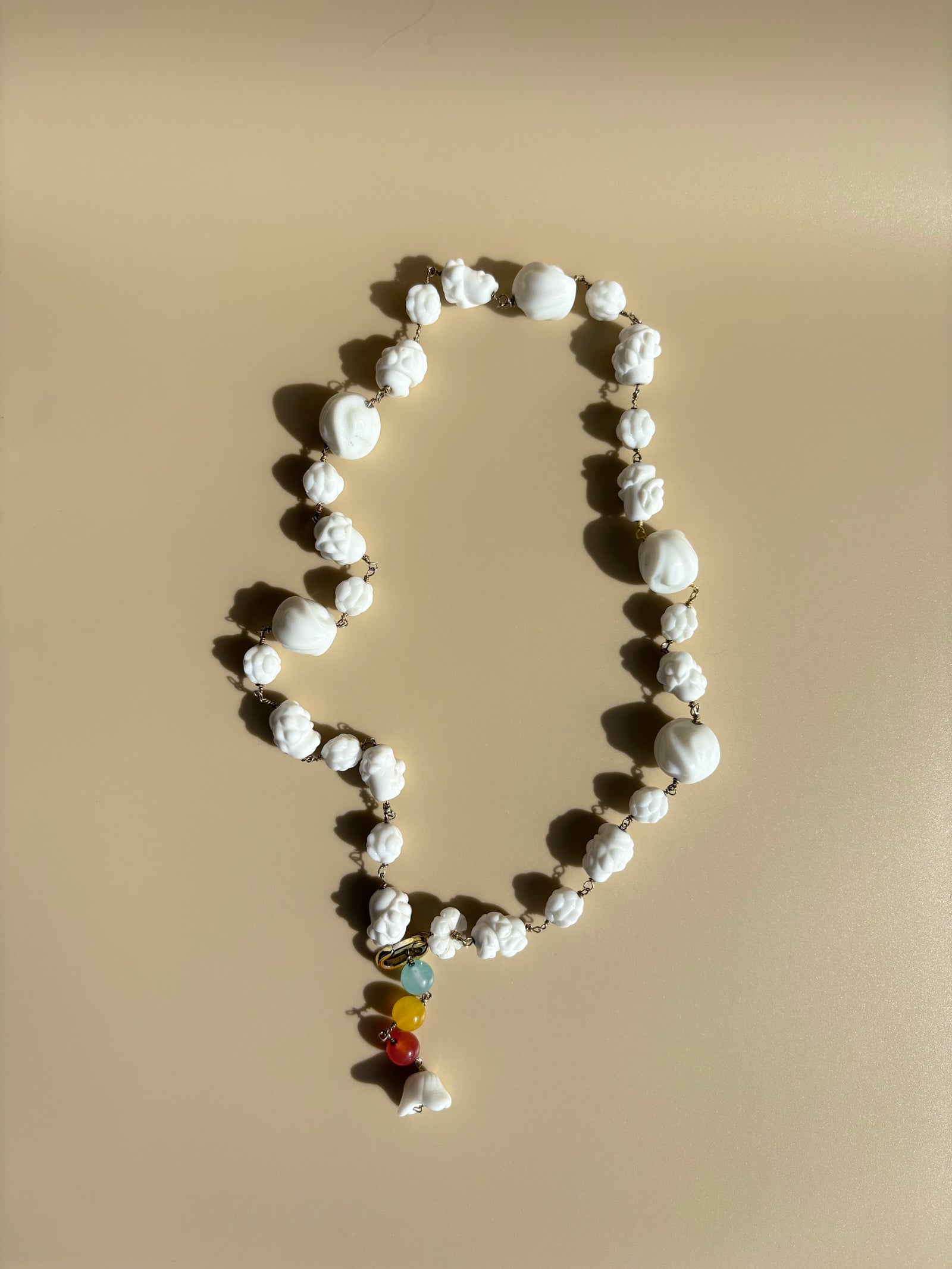 Porcelain and rainbow quartz necklace displayed on beige surface. One-of-a-kind ethical jewelry symbolizing artistry and strength.