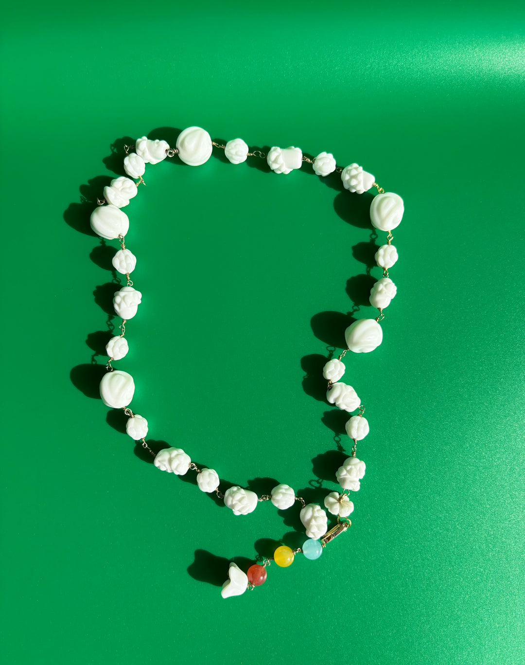 Czech porcelain and rainbow colored dyed quartz necklace laid flat on green background. Survivor-made ethical jewelry celebrating resilience.