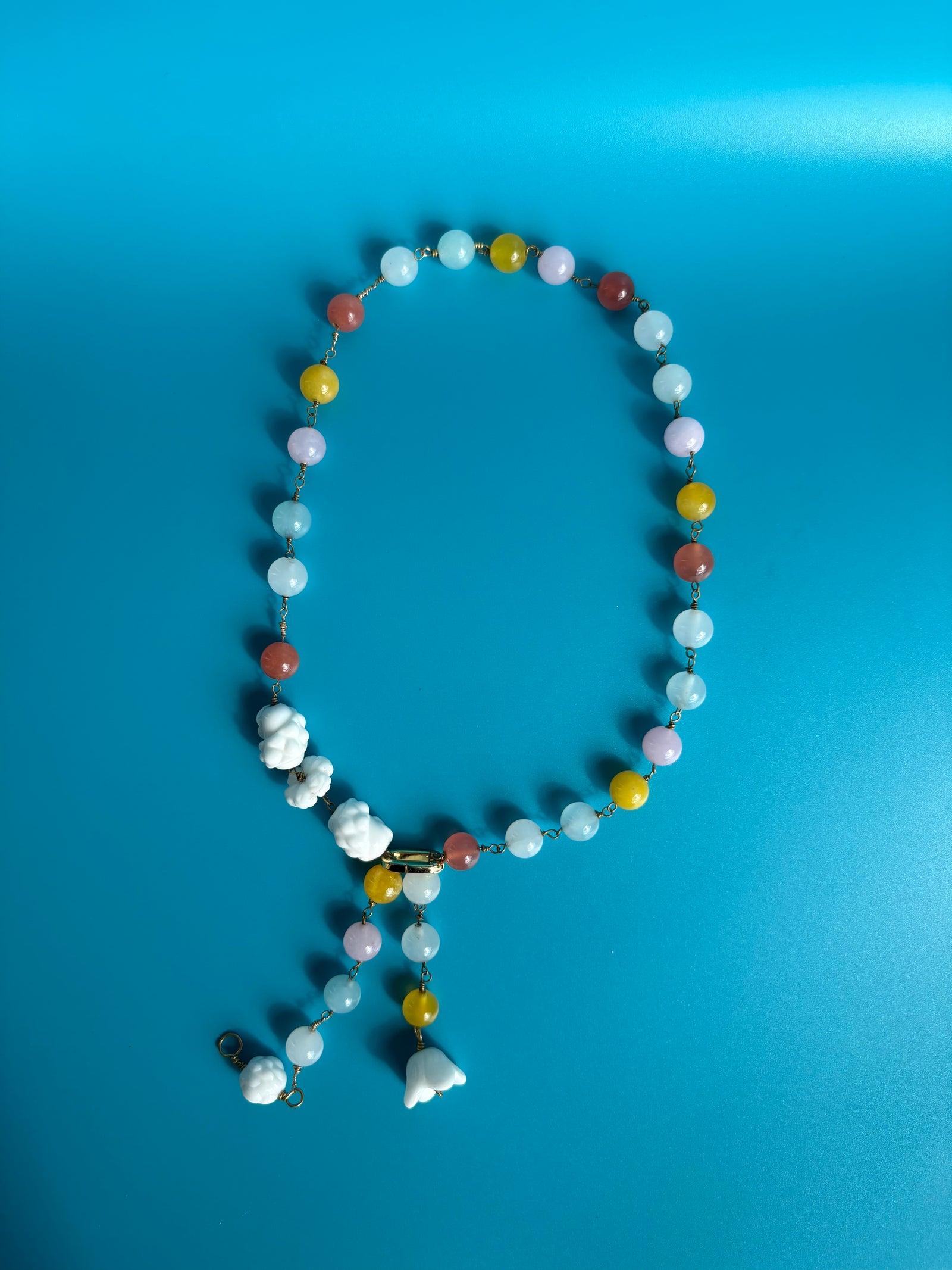 Rainbow quartz and porcelain necklace shown on blue background. Survivor-made ethical jewelry representing remembrance.