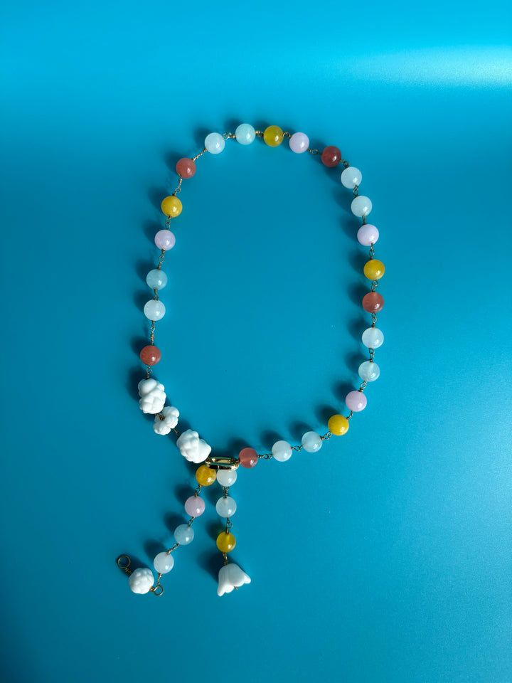 Rainbow quartz and porcelain necklace shown on blue background. Survivor-made ethical jewelry representing remembrance.