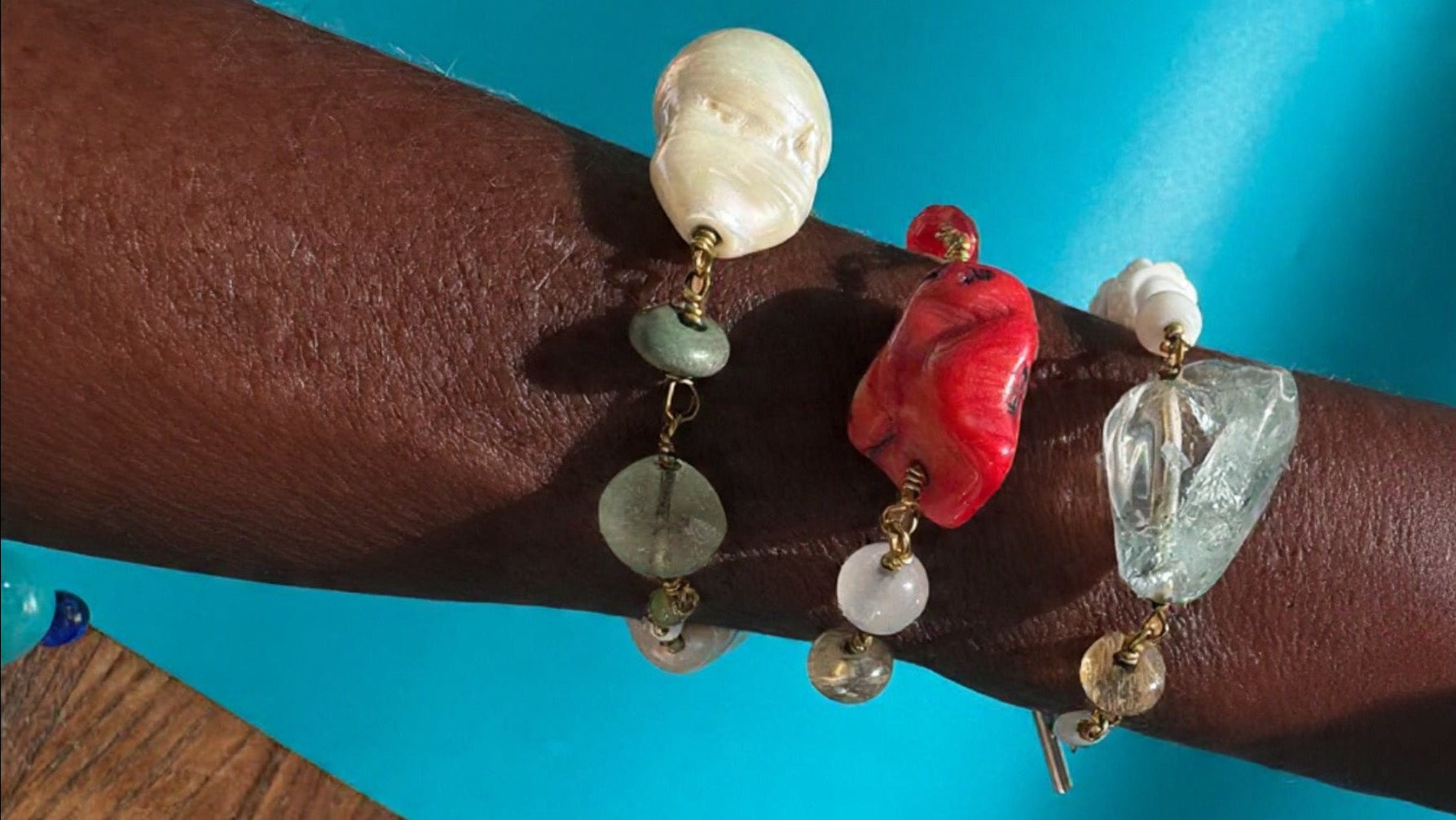 Close-up of a wrist wearing a bracelet with various beads against a blue background
