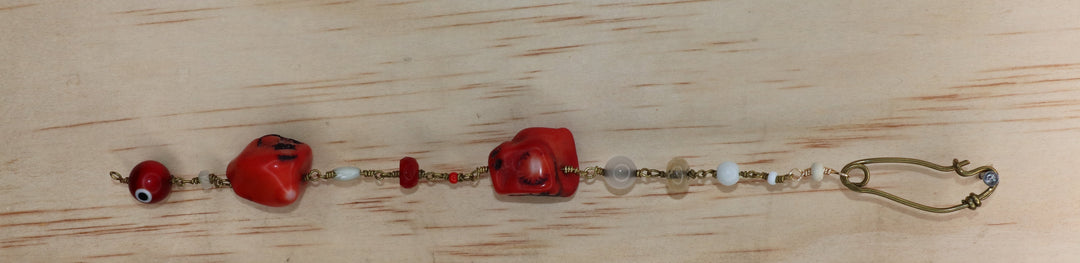 Viola bracelet featuring a gold-toned safety-pin clasp, multicolored accent beads, and sculptural red coral pieces, displayed vertically on a light wood background.